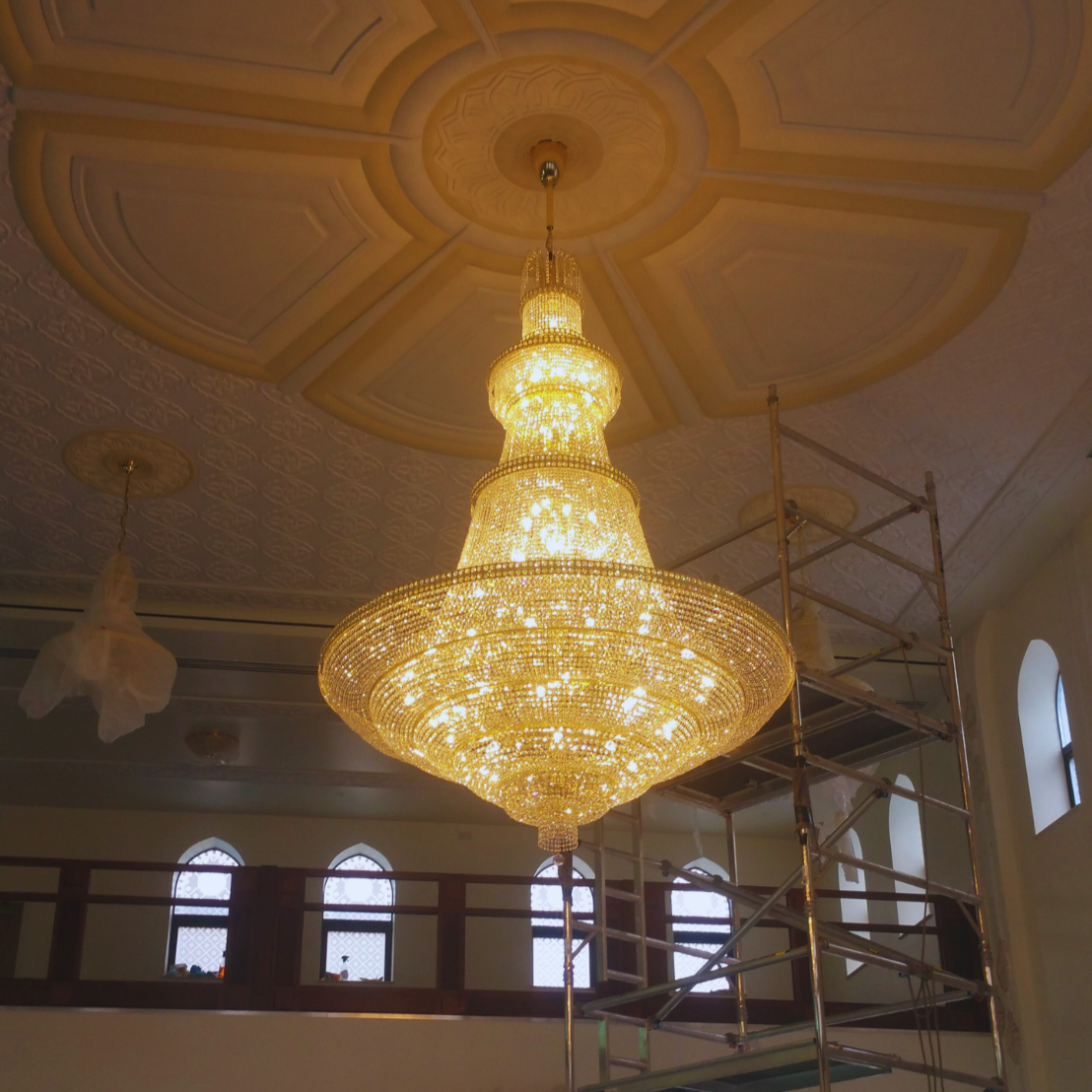 Close-up view of a grand mosque chandelier, installed with scaffolding setup.