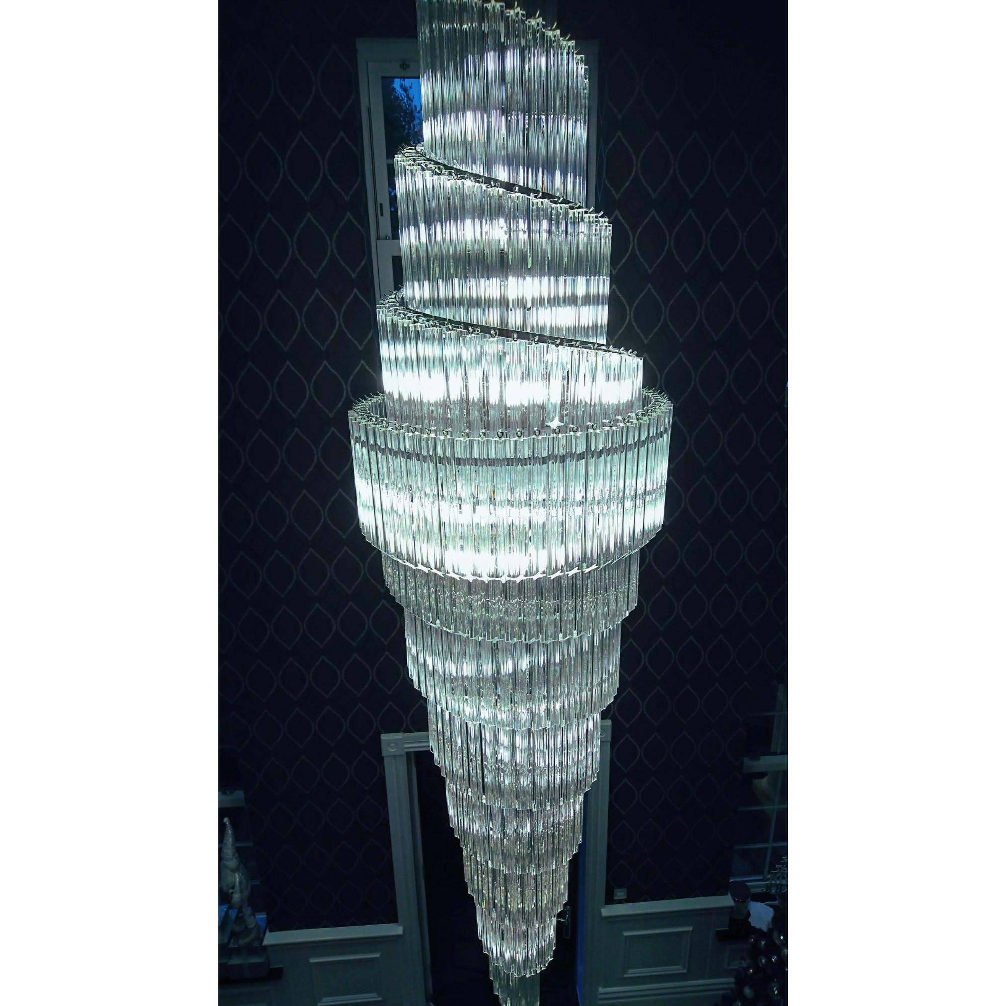 Close-up view of the spiral chandelier with layered glass design, glowing in a contemporary hallway.