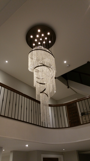 Elegant Asymmetric Crystal Spiral chandelier hanging from a high ceiling, illuminating a grand staircase