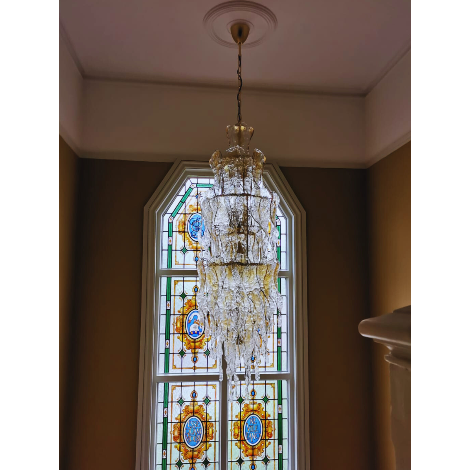 Ornate Murano glass chandelier in a grand stairwell setting with vibrant stained glass backdrop