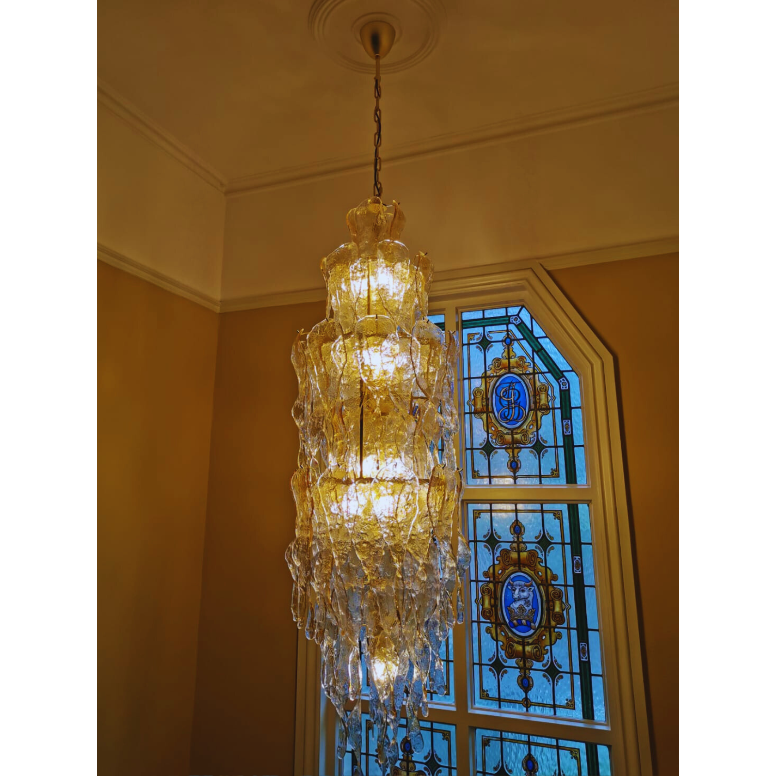 Elegant chandelier with amber icicle-like Murano glass prisms in front of stained glass window