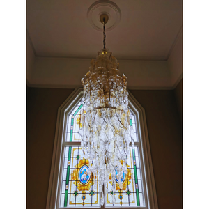 Ornate Murano glass chandelier in a grand stairwell setting with vibrant stained glass backdrop