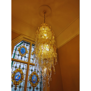 Elegant chandelier with amber icicle-like Murano glass prisms in front of stained glass window