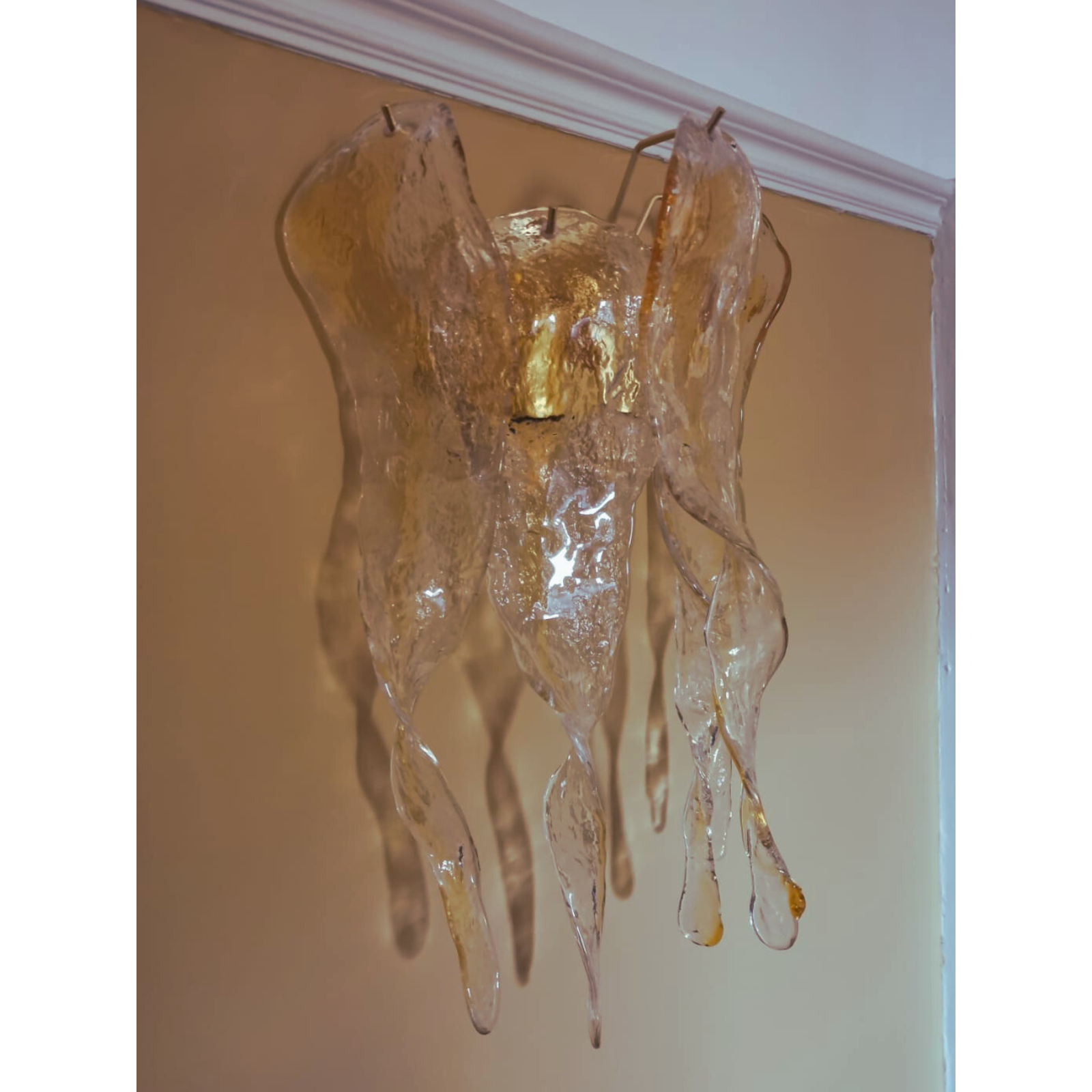 Golden amber wall-mounted Murano glass light fixture with icicle details on a patterned wall