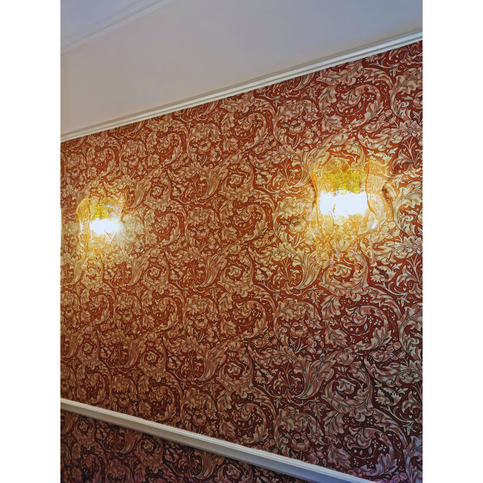 Pair of amber Murano glass sconces illuminating hallway with ornate wallpaper.