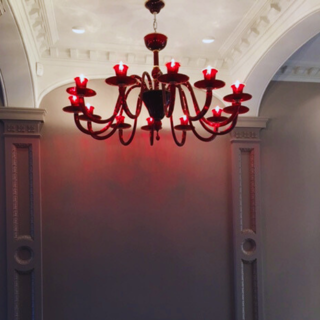 12 Arm Red Murano Chandelier with hand-blown glass design, elegantly installed in a modern interior space, showcasing bold red hues and artistic craftsmanship