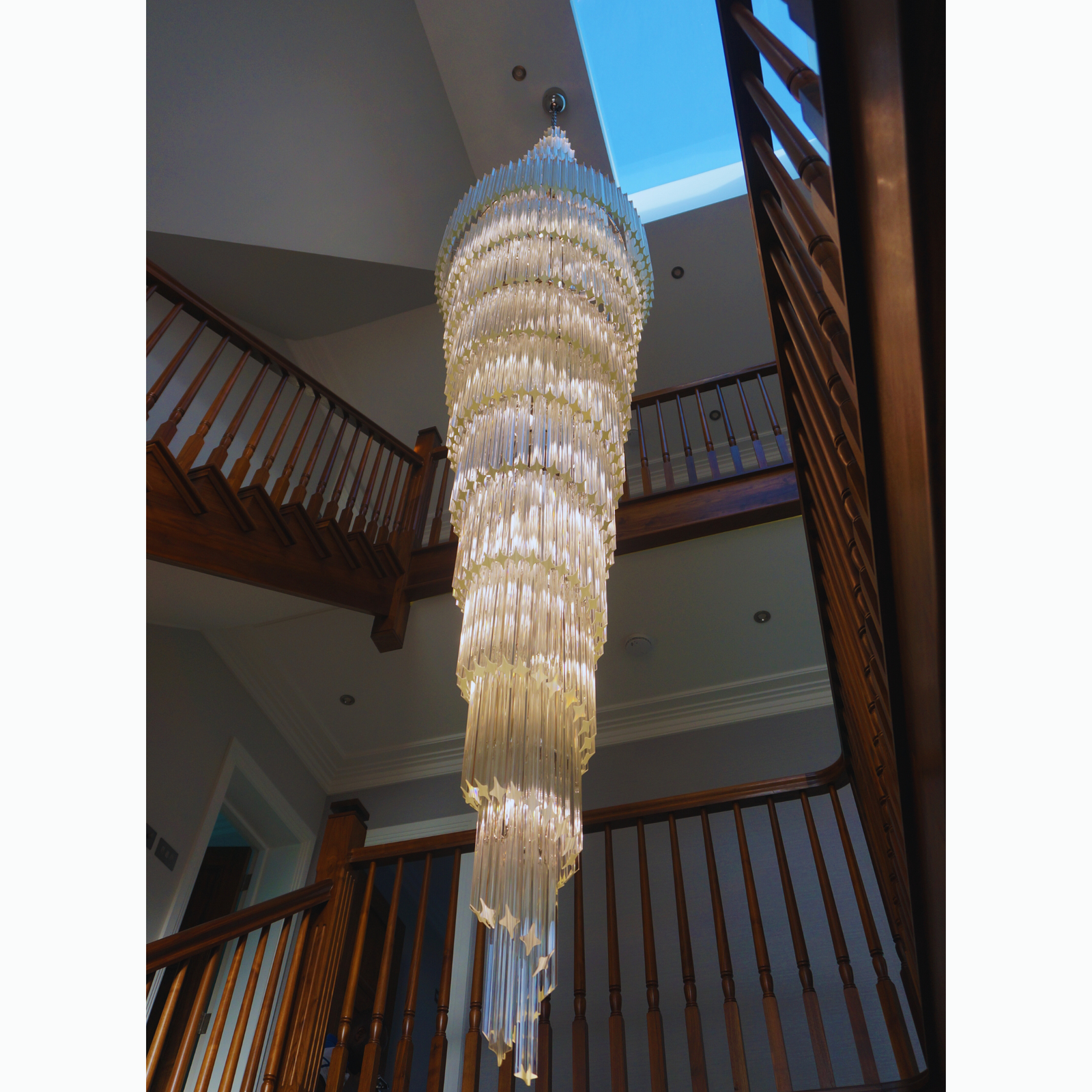 Elegant double prism chandelier showcased under a skylight, illuminating the staircase area with cascading light.