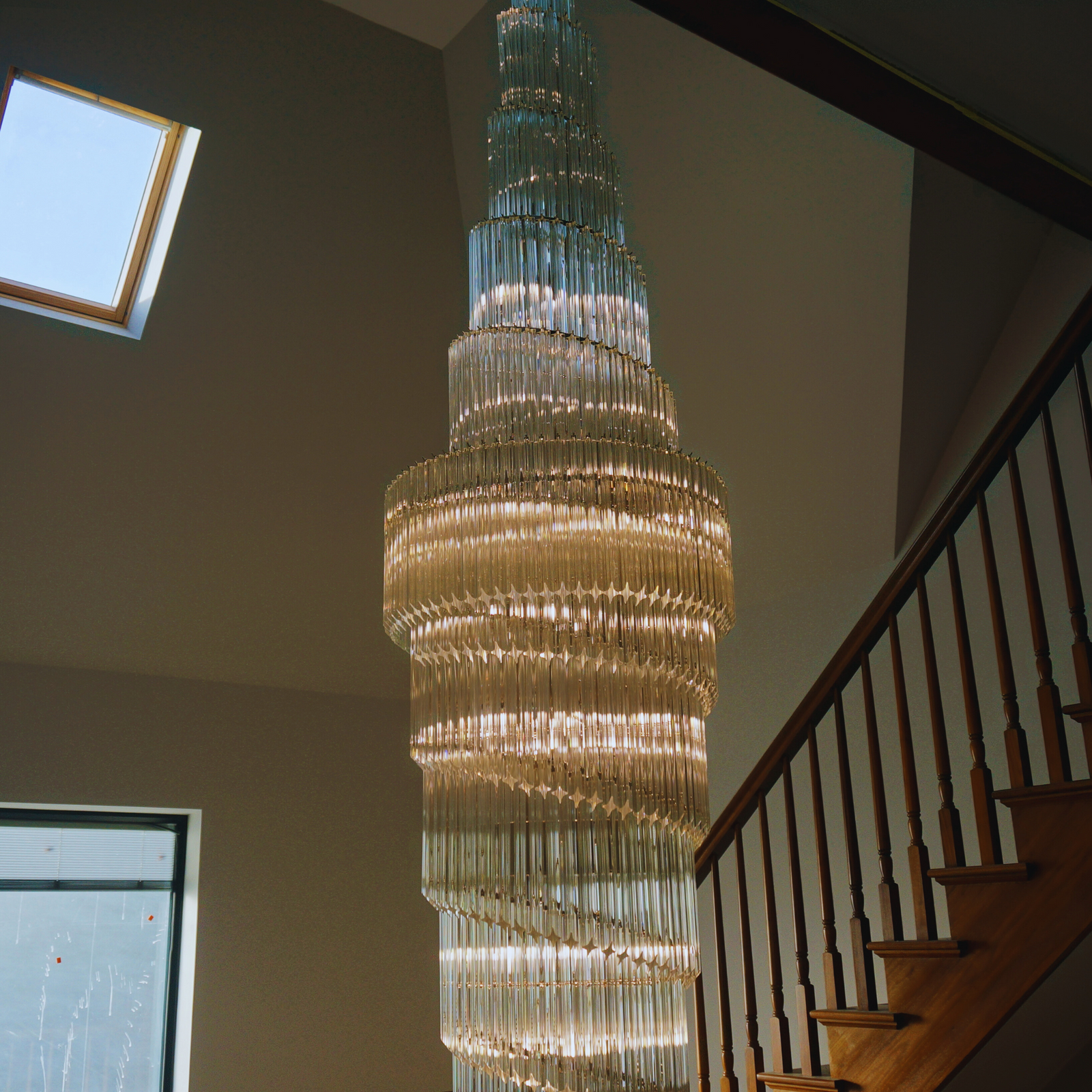 Elegant double prism chandelier showcased under a skylight, illuminating the staircase area with cascading light.
