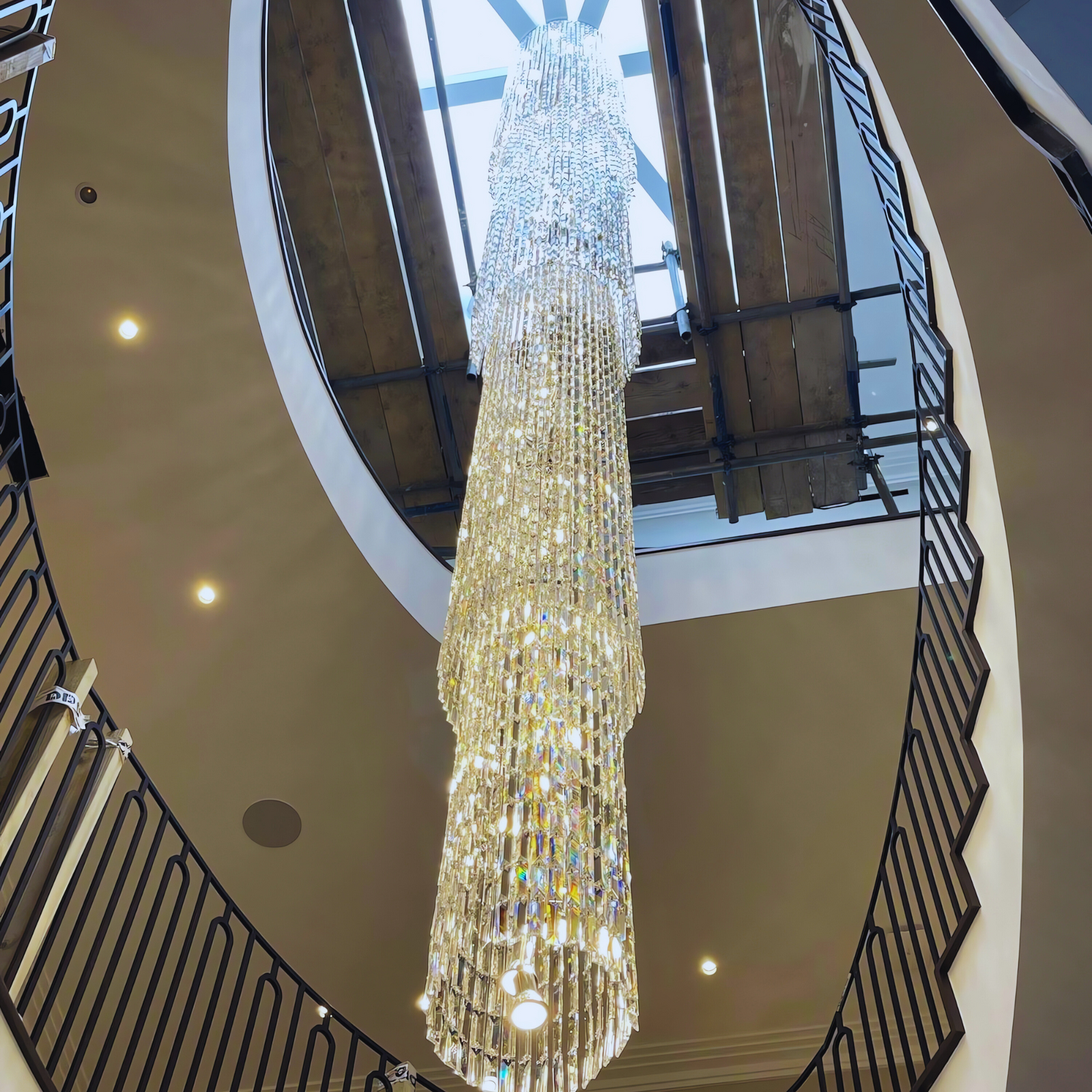 Elegant long crystal chandelier installed in a grand spiral staircase, highlighting cascading crystals and modern design.