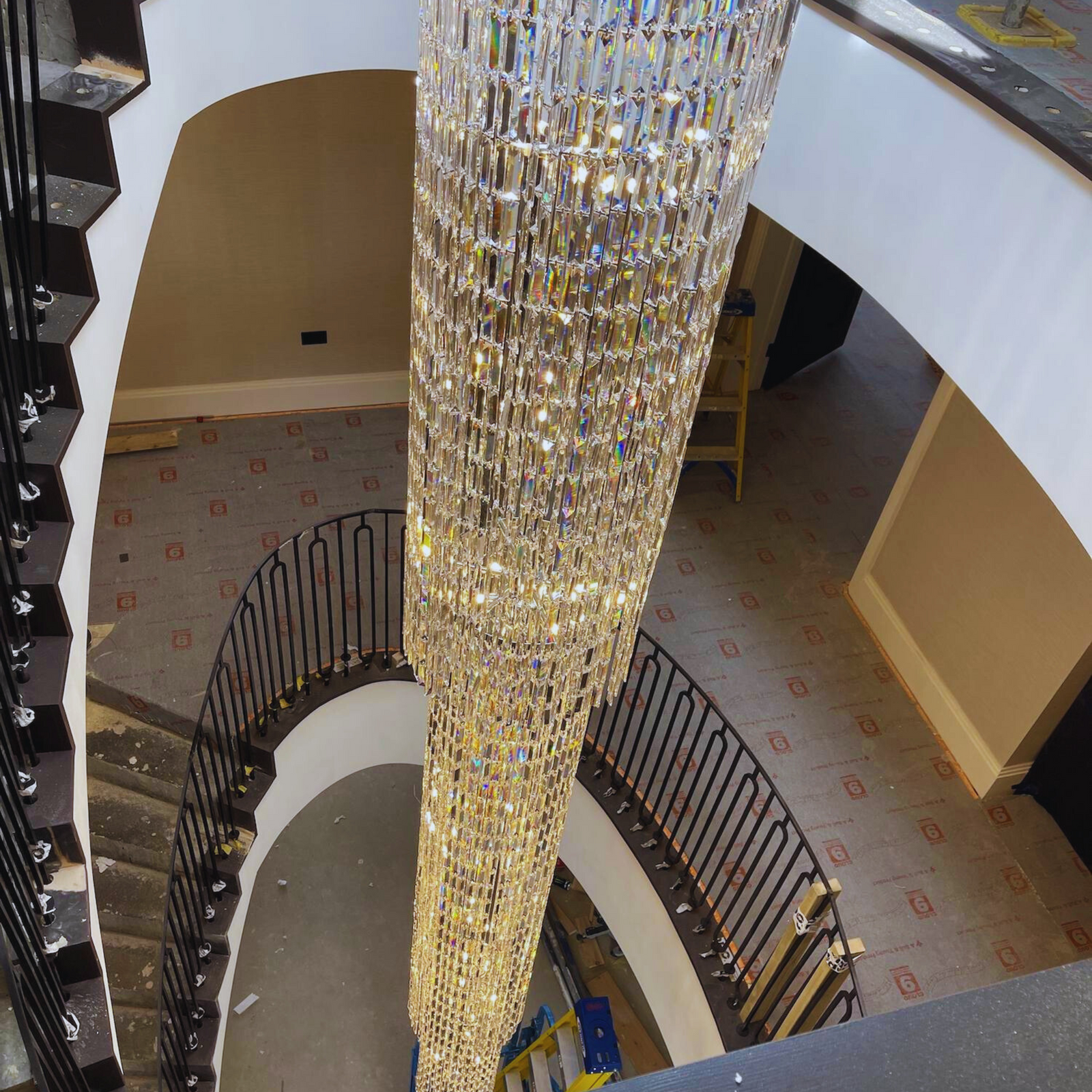 Elegant long crystal chandelier installed in a grand spiral staircase, highlighting cascading crystals and modern design.